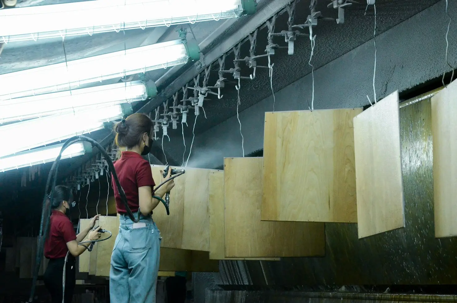 Workers spray finishing wooden panels in a furniture manufacturing factory